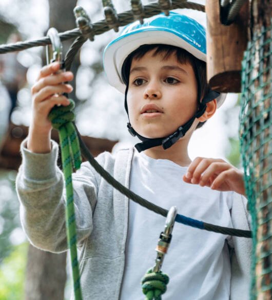 Attentive boy hooks a carbine on a rope. The boy is standing on a suspension road