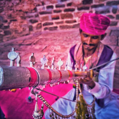man-traditional-clothing-sitting-with-musical-instrument-against-wall