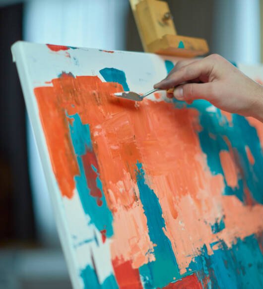 Artist's hand putting paints on canvas, add details to abstract modern painting by palette knife, creating masterpiece. Closeup. High quality photo