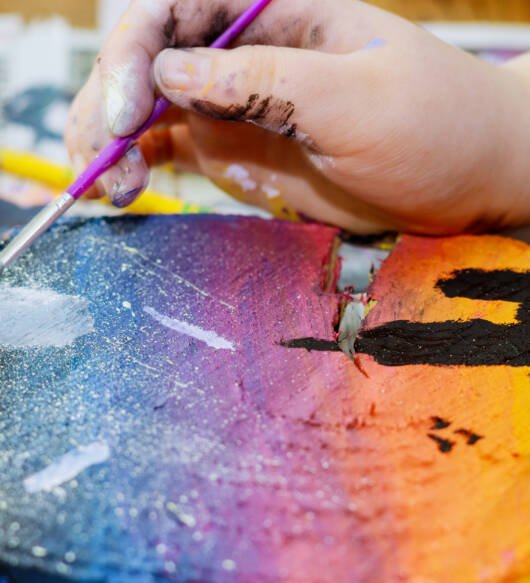 Girl draws uses colored paints brushes a picture in wooden