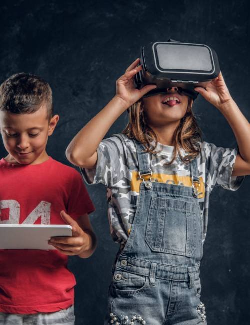 Happy smiling boy is holding tablet while funny girl is wearing vr goggles.