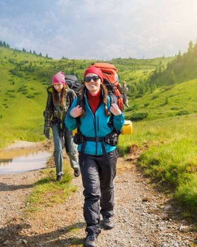 girl tourist with a backpack happy woman hiker with backpack trekking on trail in mountains. Girl tourist walking on dirt road in forest. Healthy lifestyle adventure, camping on hiking trip