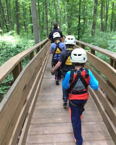 kids-walking-along-bridge-their-way-zip-line-course kids-walking-along-bridge-their-way-zip-line-course