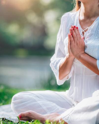 Meditation by the water, hands in prayer position, green background.