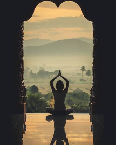 Yoga woman sitting in lotus pose on the temple during sunrise, with reflection in floor - vintage style color effect